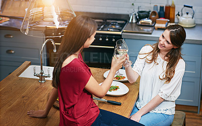 Buy stock photo Shot of two friends sitting at the kitchen table eating pizza and drinking wine