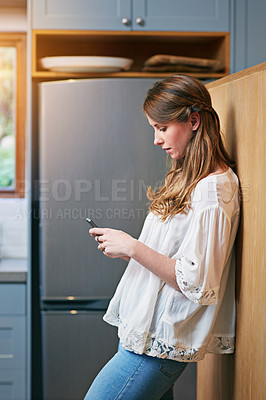 Buy stock photo Shot of a young woman using a cellphone in the kitchen