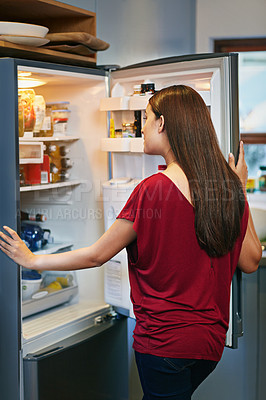 Buy stock photo Shot of a young woman standing by an open fridge in her kitchen