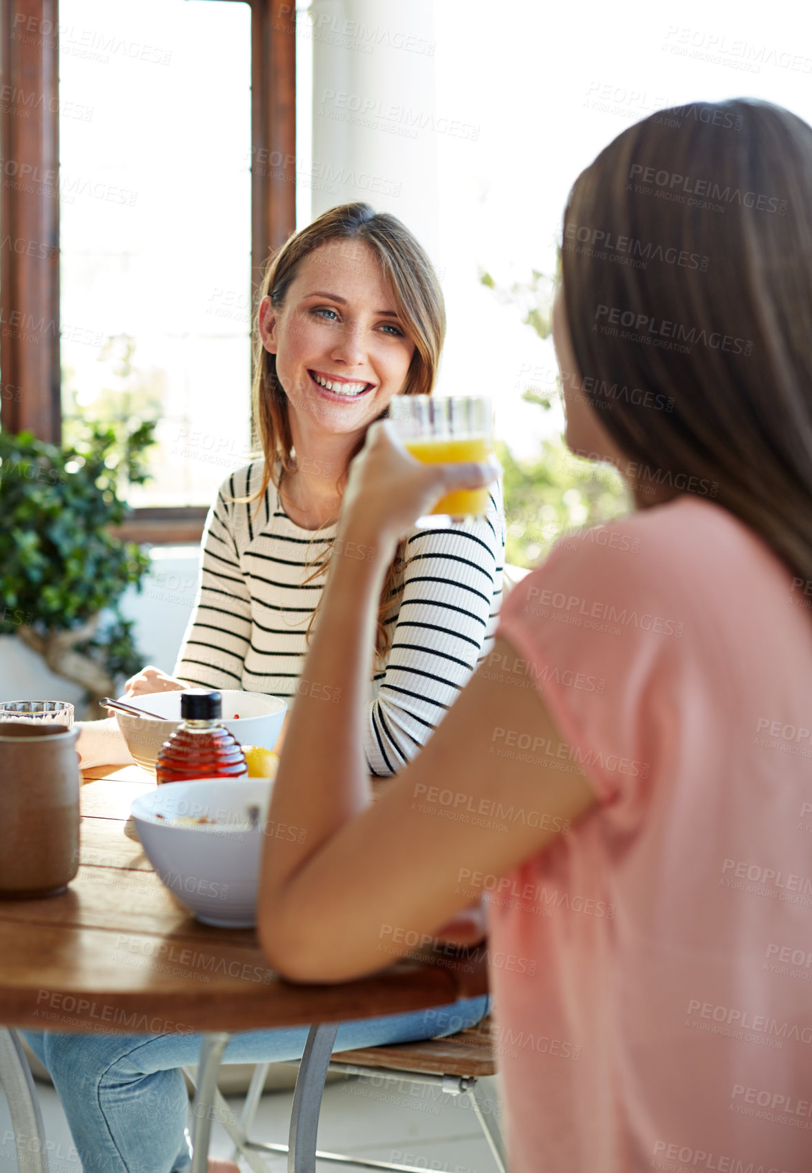 Buy stock photo Shot of two friends eating breakfast together on a balcony