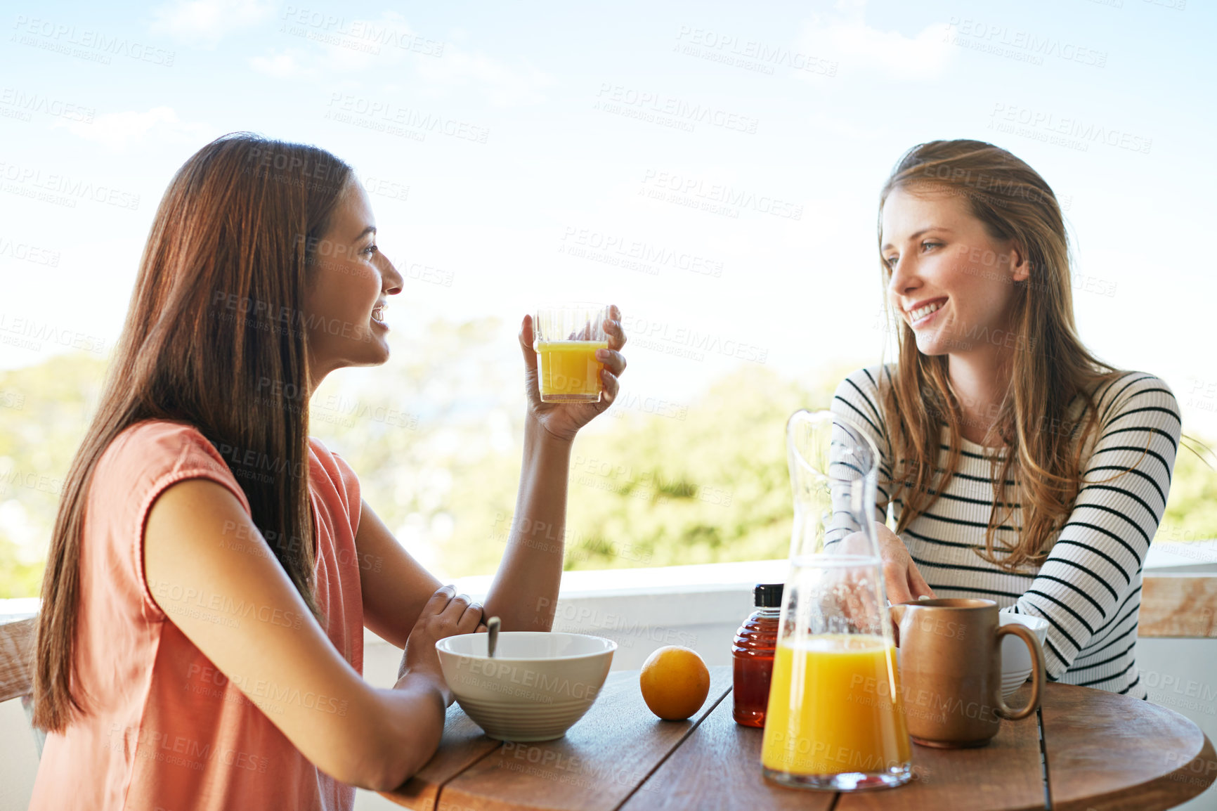 Buy stock photo Shot of two friends eating breakfast together on a balcony