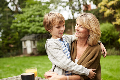 Buy stock photo Shot of a grandmother and her grandson hugging while sitting at a table in her yard