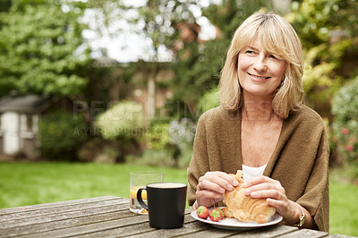 Buy stock photo Shot of a mature woman sitting in her yard eating breakfast
