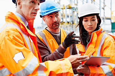 Buy stock photo Shot of three workers talking together over a digital tablet while standing on a commercial dock