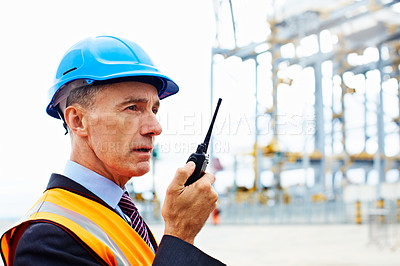 Buy stock photo Shot of a man in workwear standing outside on a large commercial dock talking on a walkie talking