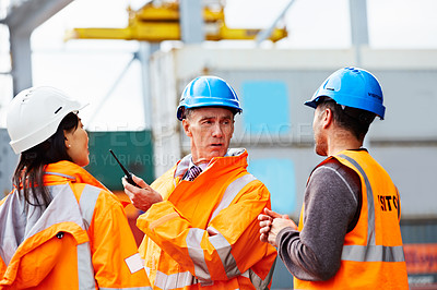 Buy stock photo Shot of three workers talking while standing on a commercial dock