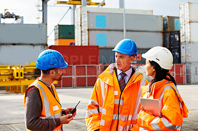 Buy stock photo Shot of three workers talking while standing on a commercial dock
