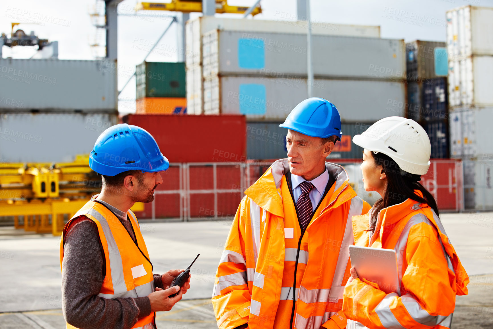 Buy stock photo Shot of three workers talking while standing on a commercial dock