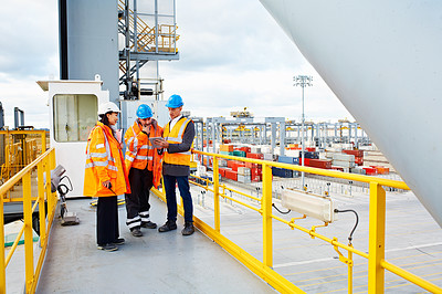 Buy stock photo Shot of three workers talking together over a digital tablet while standing on a commercial dock