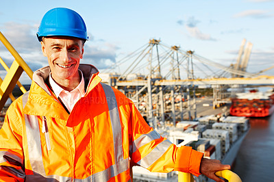 Buy stock photo Portrait of a man in workwear standing on a walkway looking out over at a large commercial dock