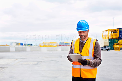 Buy stock photo Shot of a young man in workwear using a digital tablet while standing on a large commercial dock