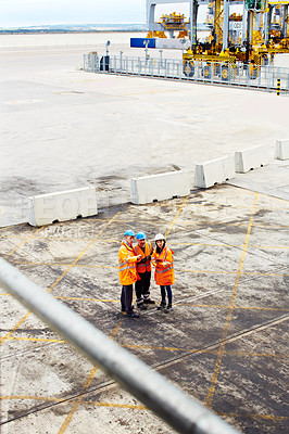 Buy stock photo High angle shot of three workers talking together while standing on a commercial dock