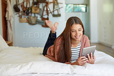 Buy stock photo Shot of a young woman lying on her bed using a digital tablet