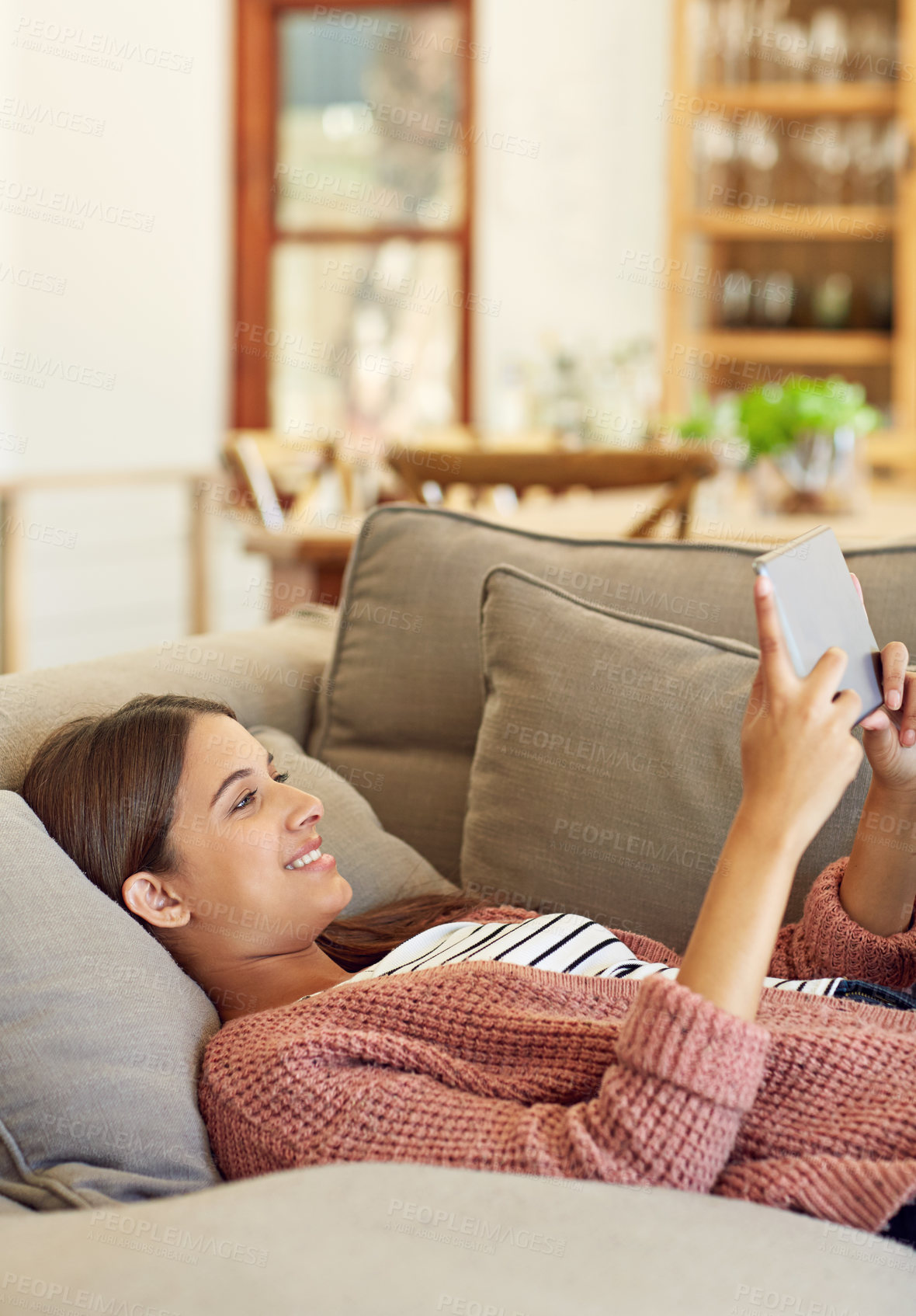 Buy stock photo Shot of a young woman lying on her sofa using a digital tablet