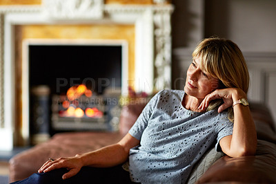 Buy stock photo Shot of a mature woman relaxing on her living room sofa with a fire glowing in the background