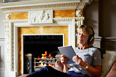 Buy stock photo Shot of a mature woman sitting on her sofa using a digital tablet