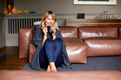 Buy stock photo Shot of a mature woman sitting on her living room floor  drinking tea while wrapped in a blanket