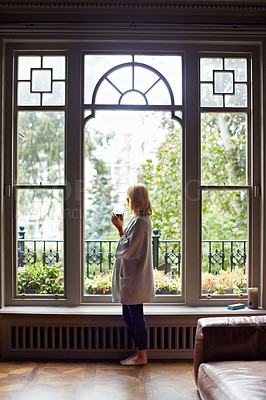Buy stock photo Shot of a mature woman drinking tea while looking out of her living room window
