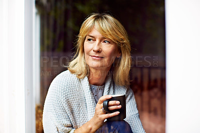 Buy stock photo Shot of a mature woman drinking coffee while looking out of her living room window
