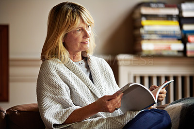 Buy stock photo Shot of a mature woman reading a book while sitting on her sofa