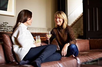 Buy stock photo Shot of two women sitting on a sofa drinking wine and talking