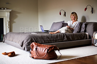 Buy stock photo Shot of a mature businesswoman lying on a hotel bed using a digital tablet