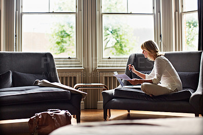 Buy stock photo Shot of a mature woman working on a laptop in her living room after a trip