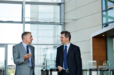 Buy stock photo Shot of two businessman talking together while walking through an office building lobby