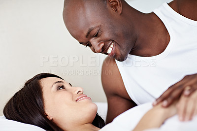 Buy stock photo Shot of a young couple laughing while lying in bed together
