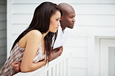 Buy stock photo Shot of a young couple leaning on the railing of their balcony