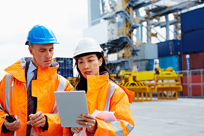 Buy stock photo Shot of two dock workers looking at a tablet while standing in a dockyard