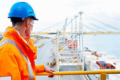 Buy stock photo Shot of a man in workwear standing on a walkway looking out over at a large commercial dock