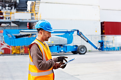 Buy stock photo Shot of a young man in workwear using a digital tablet while standing on a large commercial dock