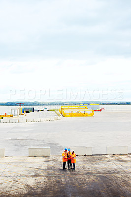 Buy stock photo High angle shot of three workers talking together while standing on a commercial dock