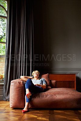 Buy stock photo Shot of a mature woman sitting back on her sofa listening to music on headphones