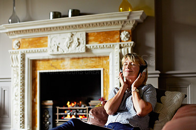 Buy stock photo Shot of a mature woman lying back on her sofa listening to music on headphones