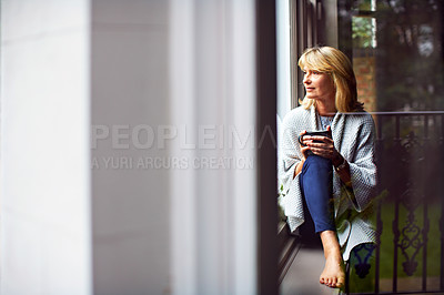 Buy stock photo Shot of a mature woman drinking tea while looking out of her living room window