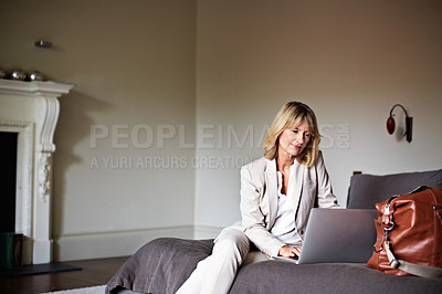 Buy stock photo Shot of a mature businesswoman using her laptop while sitting on her hotel bed