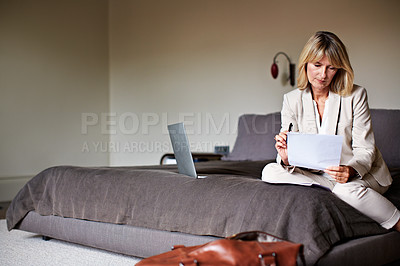 Buy stock photo Shot of a mature businesswoman going over some paperwork while sitting on her hotel bed