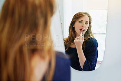 Buy stock photo Shot of a young woman putting on lipstick in her bathroom mirror