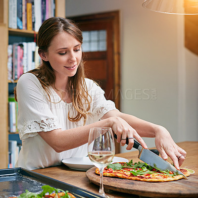 Buy stock photo Shot of a young woman sitting at a dining table slicing pizza and drinking wine