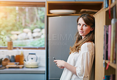 Buy stock photo Portrait of a young woman using a cellphone in the kitchen