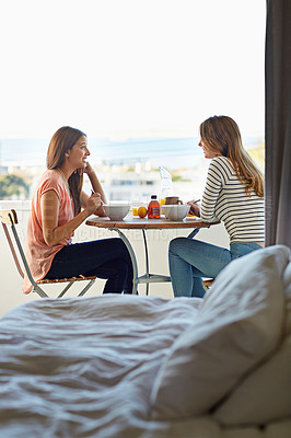 Buy stock photo Shot of two friends eating breakfast together on a balcony