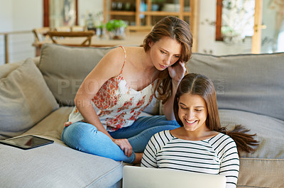 Buy stock photo Shot of two young friends sitting in the living room using a laptop together