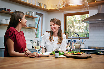 Buy stock photo Shot of two friends sitting at the kitchen table eating pizza and drinking wine