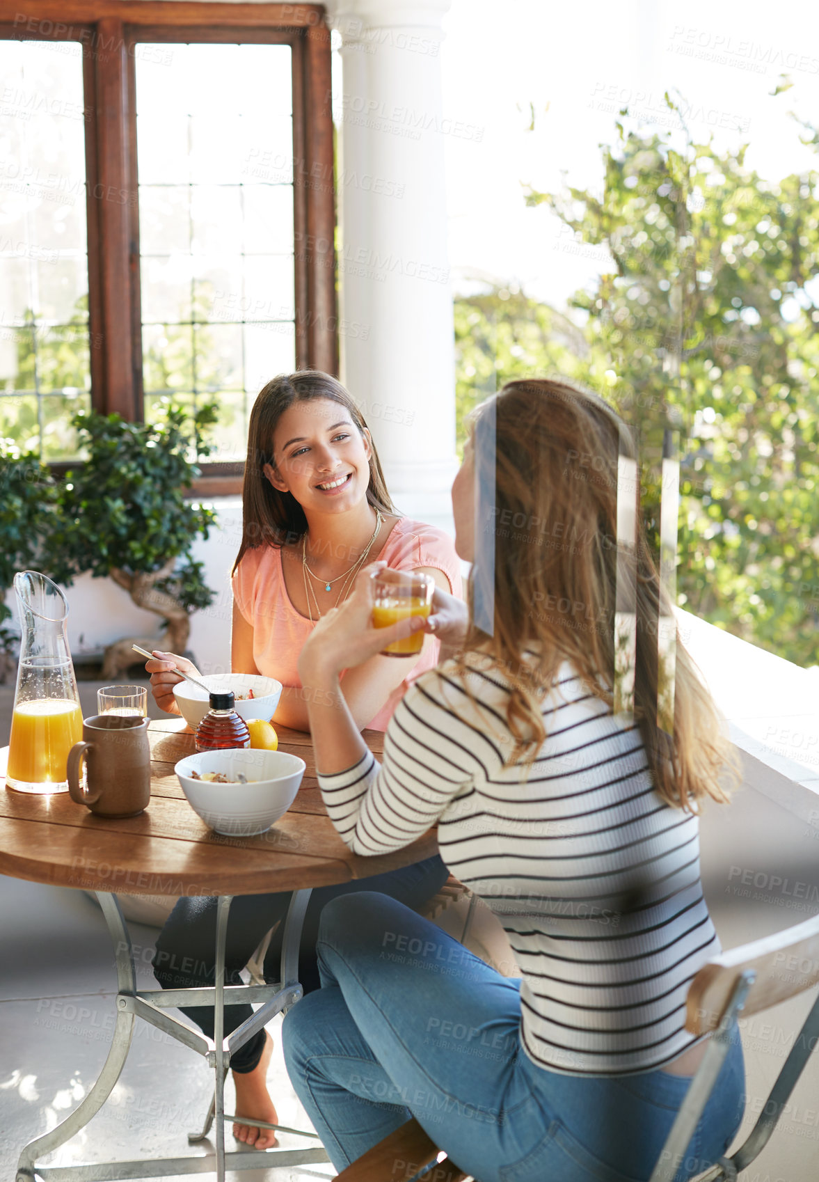 Buy stock photo Shot of two friends eating breakfast together on a balcony