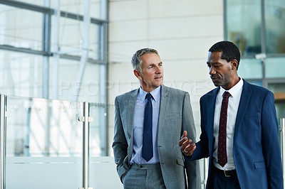 Buy stock photo Shot of two businessmen walking and talking together in the lobby of an office building