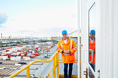 Buy stock photo Portrait of a man in workwear standing on a walkway looking  out over at a large commercial dock