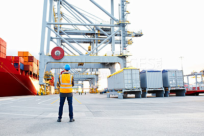 Buy stock photo Rearview shot of a man in workwear looking up at a crane on a commercial dock