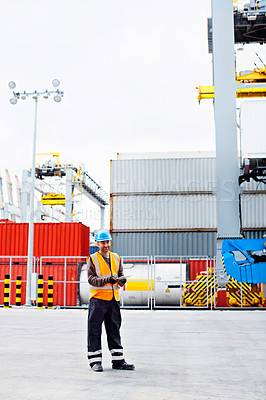 Buy stock photo Shot of a young man in workwear using a digital tablet while standing on a large commercial dock